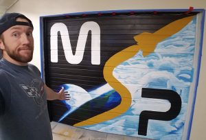 Caleb Edmonds in front of MSP mural he painted