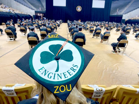 A student shows off a mortarboard decorated with the image of the three-leaf clover representing Mizzou Engineering.