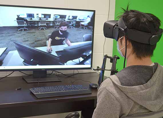 A student using VR goggles in front of a screen showing a classmate.