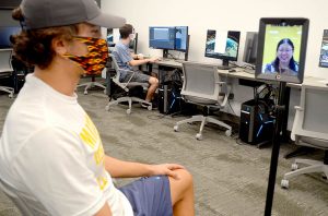Weiyu Feng uses virtual reality goggles to experience a classroom he is not physically in. Through the goggles, he can see classmate Will Slama in a realistic setting rather than on screen.