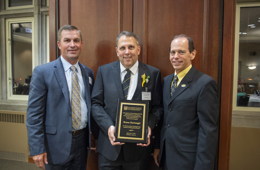 Three men in suits hold a plaque.