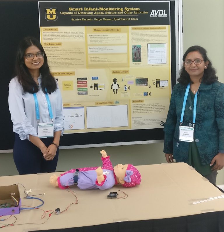 Omiya Hassan and Samira Shamsir with their research poster. In front of them is a prototype of their smart infant monitoring system.