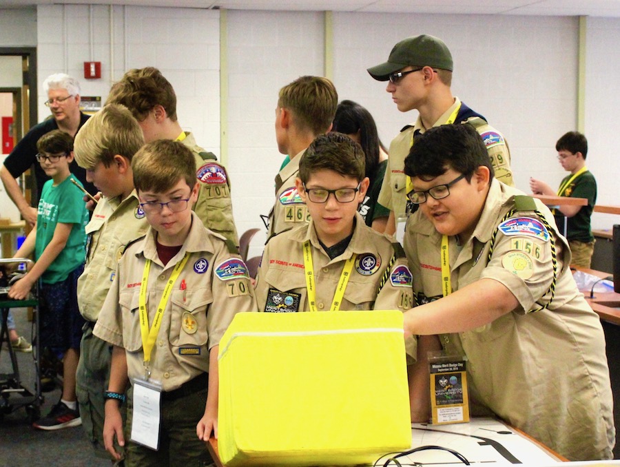 Three scouts crowd around a yellow box.