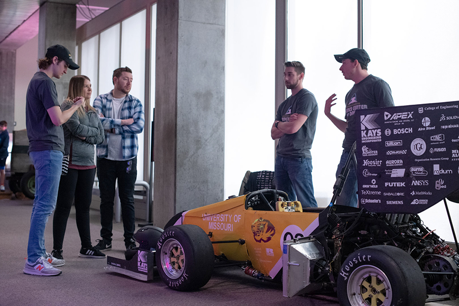 Mizzou students show off their gold race car to attendees at a science event.