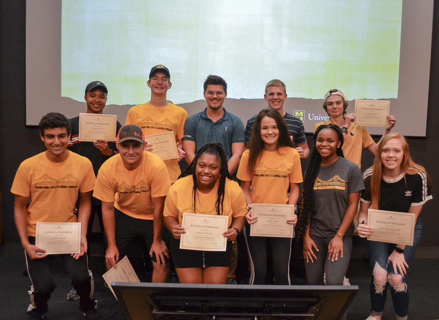 Students pose with certificates in front of a projection screen.
