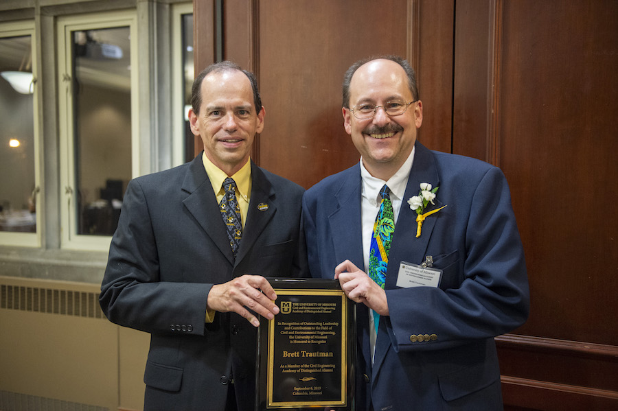 Two men in suits hold a plaque.