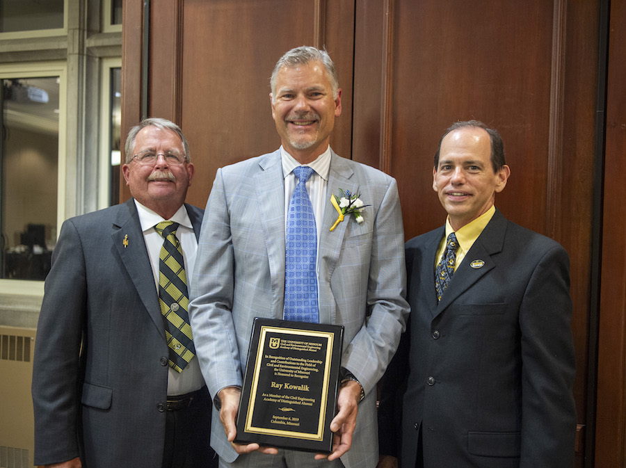 Three men in suits hold a plaque.