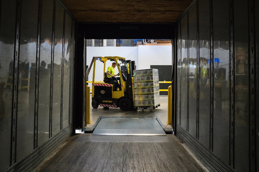 A man takes goods off a truck with a forklift.