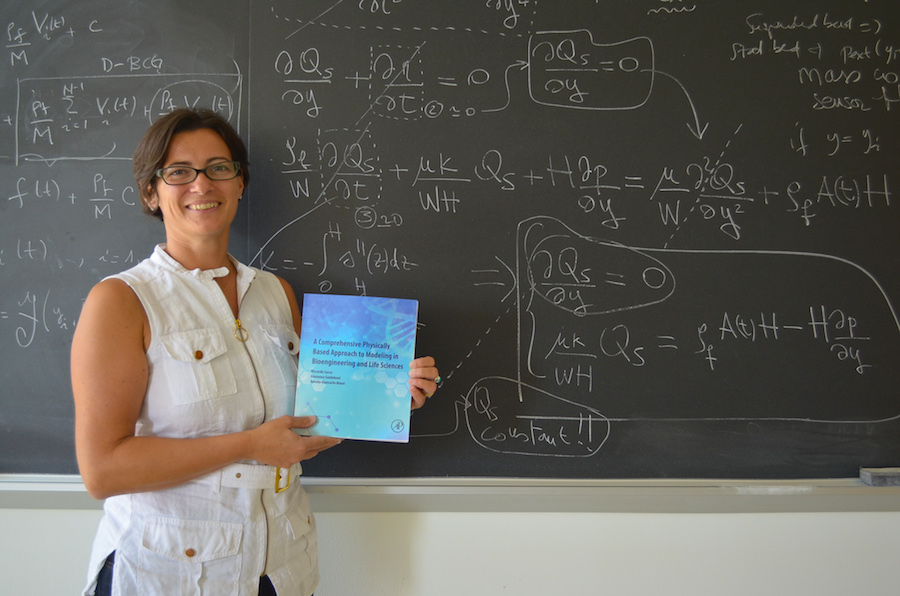 Giovanna Guidoboni presents her new textbook in front of a blackboard covered in equations