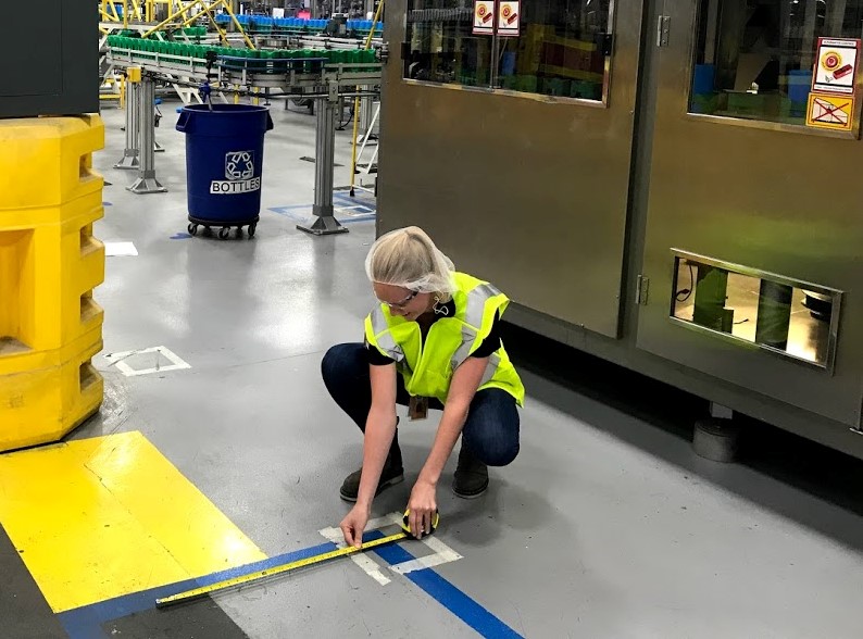 Langley measures a section of flooring while wearing a safety vest.