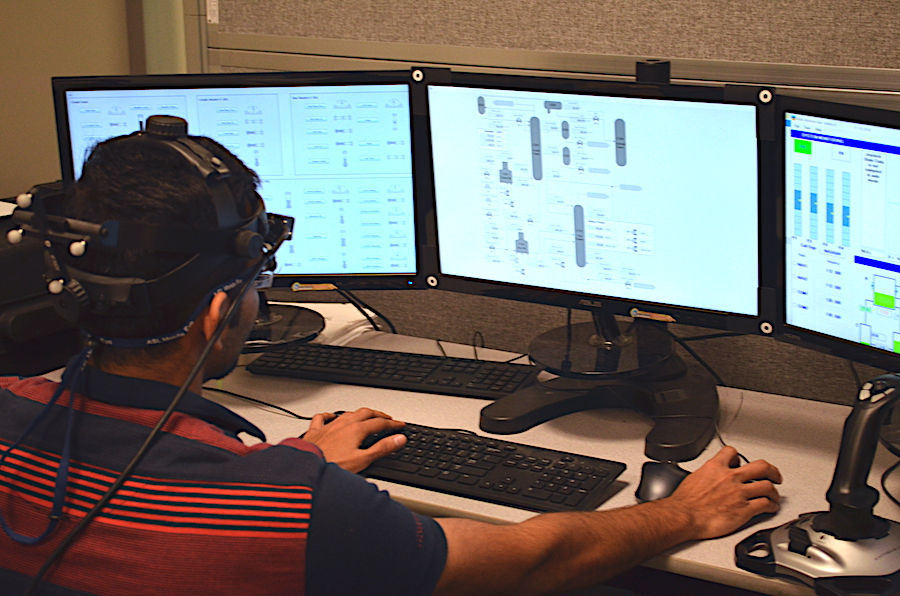 A man wearing headgear works on a three-monitor computer.