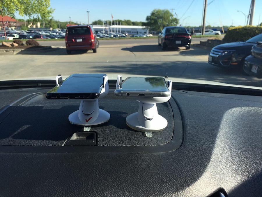 On the dashboard of a car, two mobile phones are mounted in parallel holders.