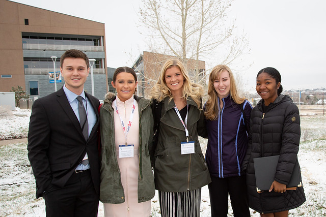 Students in coats and business attire stand in the snow.