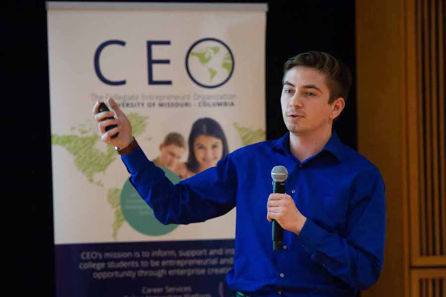 A man in a blue shirt holds a microphone and clicker.