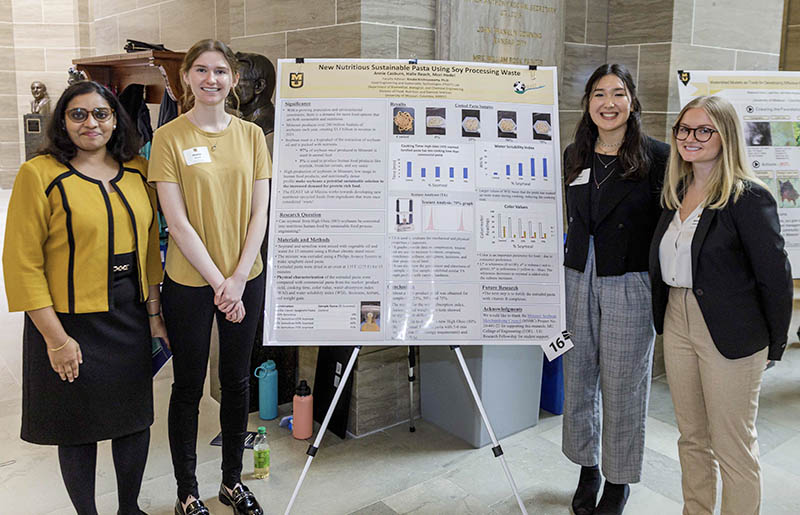 Four women in front of research poster.