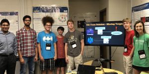 A group of students stand near a monitor.