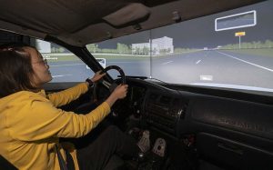 A woman in the front seat of a car looking at a simulated environment.