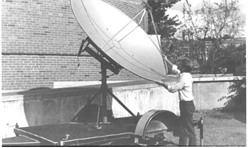 Black and white image of man working on large satellite. 