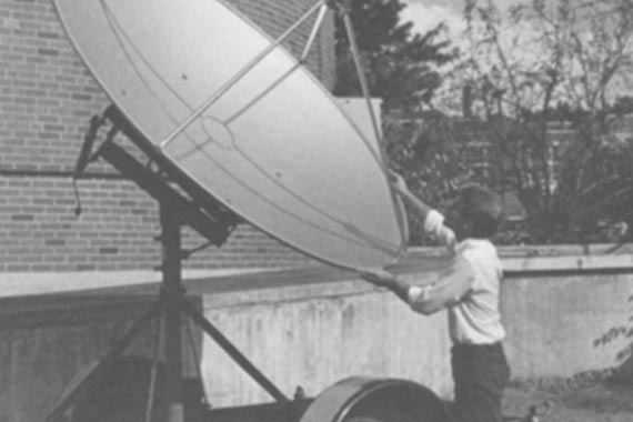 Black and white image of man working on large satellite.