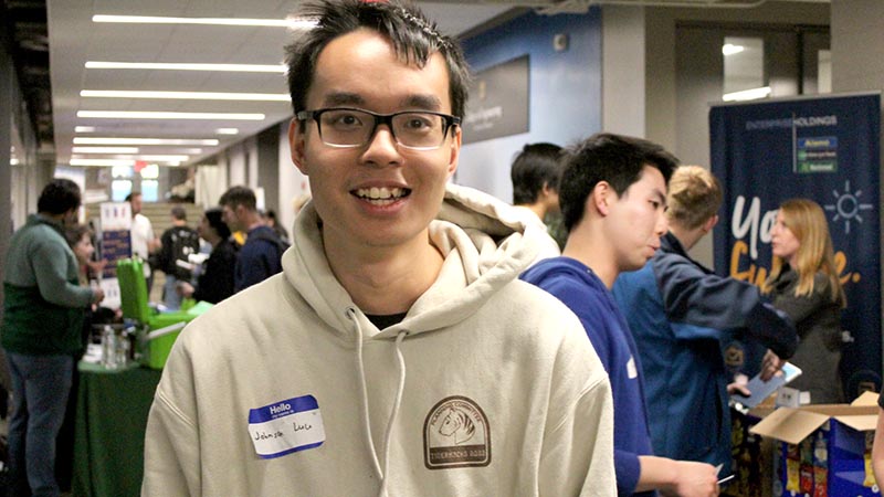 Image of Johnson Lee, a first generation college student, at TigerHacks with booths and participants behind him.