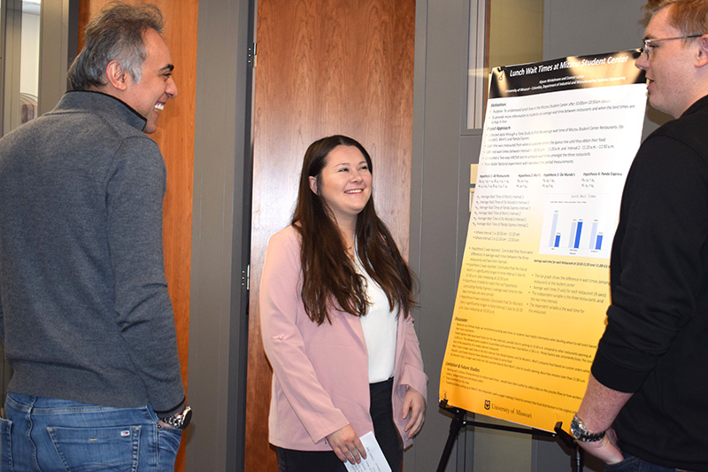Three people talk in front of research poster