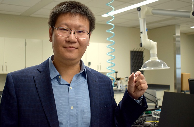 Researcher holding microprobe in his hand with lab equipment behind him