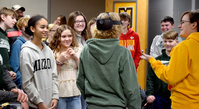 Crowd of young students watch as another student wears a VR headset.