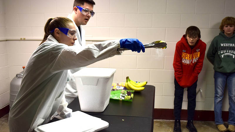 Woman in a lab coat demonstrates chemical reactions using produce.