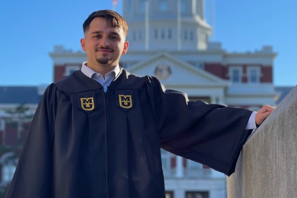 Sergio Pico-Vazquez poses in front of Jesse Hall in graduation gown.