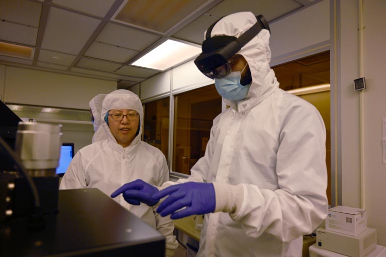 Fang Wang with student using machine in cleanroom