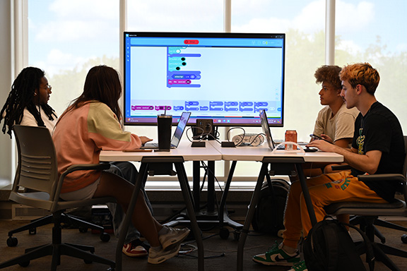 Four students sit at a table around a TV screen