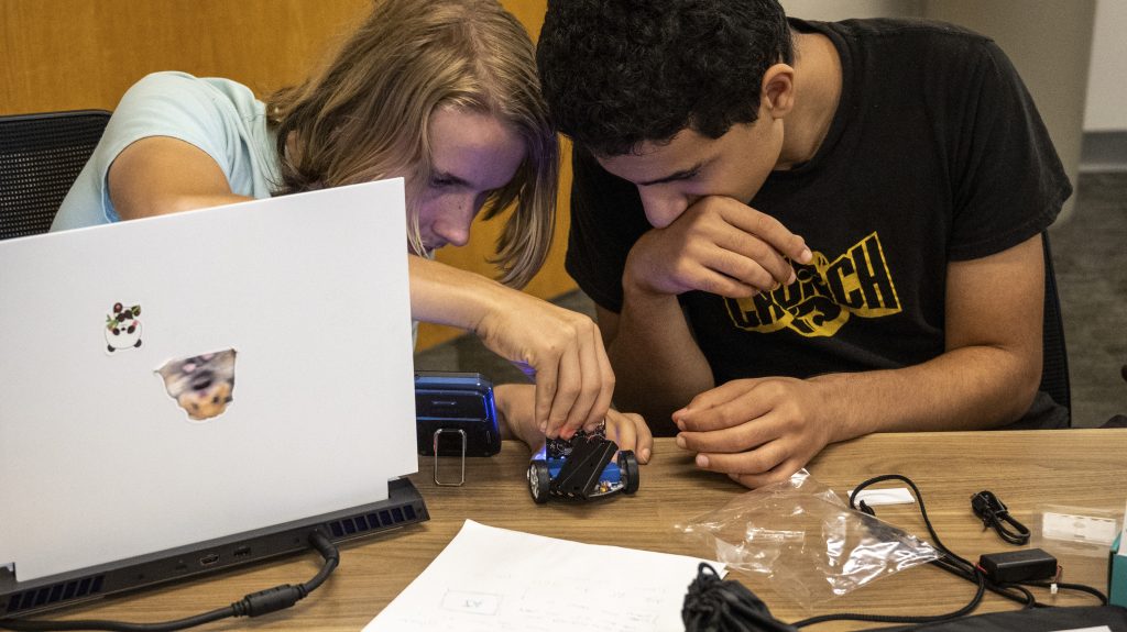 Two young men make adjustments to a miniature autonomous vehicle
