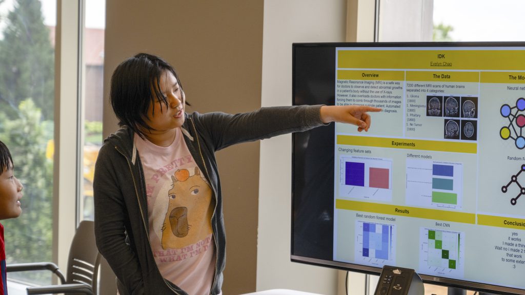 Young woman points to screen of data visualization during presentation