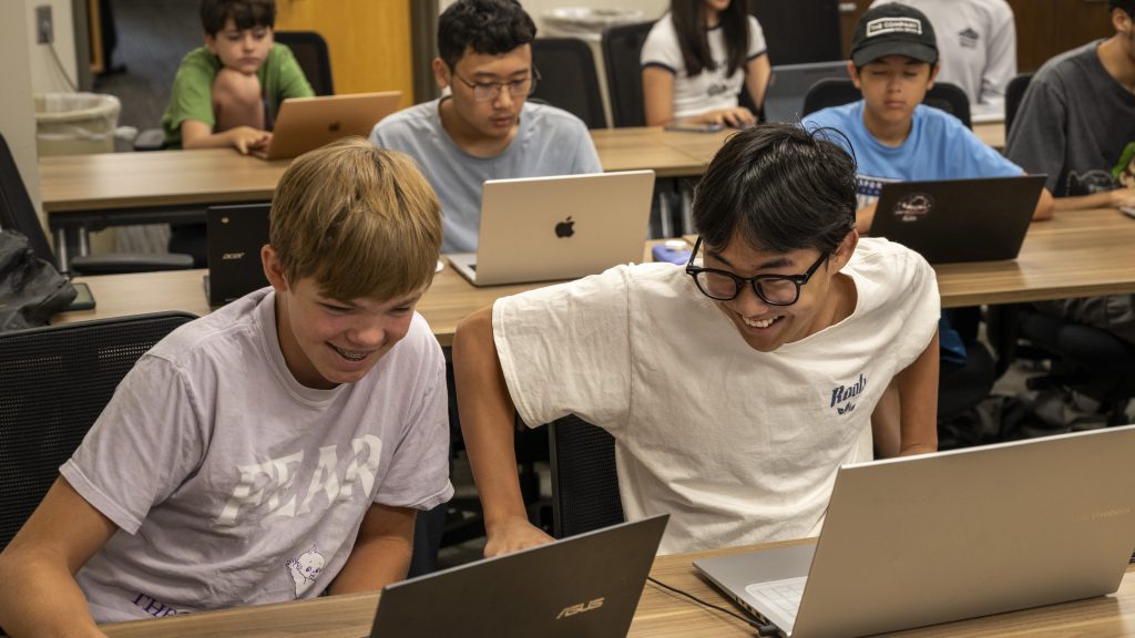 Two young men laughing and looking at their laptop computers