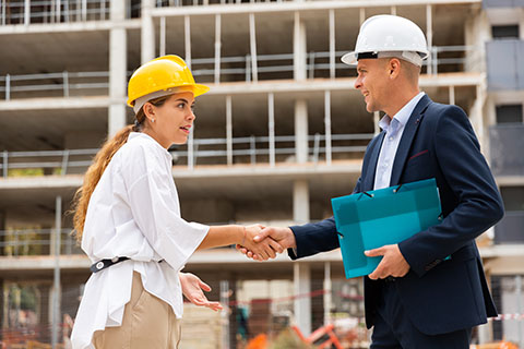Woman shakes a hand of a man, both wearing hard hats