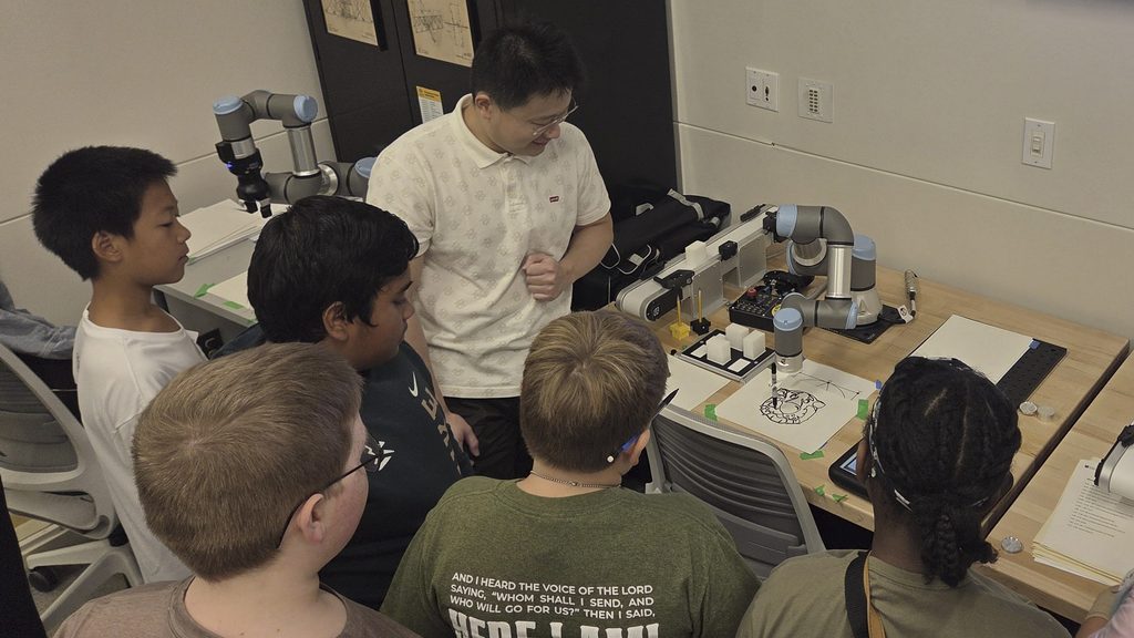 Students observe as a manufacturing robot draws a picture of Truman the Tiger.