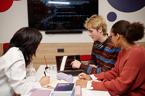 Three students sitting in front of a large TV with code on it