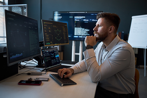 Caucasian young adult man analyzing cybersecurity data on multiple monitors in office