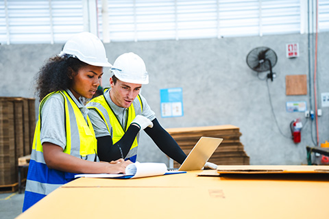 Female engineer using laptop computer for safety control checks or manufacturing maintenance work in factory building or construction site