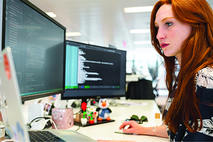 Woman sits working on a computer with two monitors